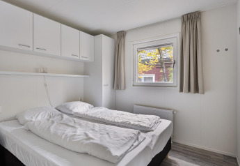 Dormitorio con dos camas individuales, armarios blancos y ventana en Wellness Lodge de De Thijmse Berg, Países Bajos.