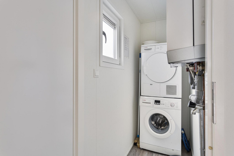 Compact laundry room with stacked washer and dryer at Wellness Lodge | 2 persons, De Thijmse Berg, Netherlands.