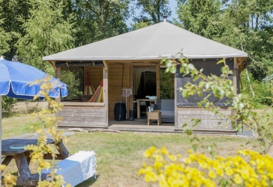 Houten lodge genaamd Camphome met overdekte veranda en hangmat, op gras en omringd door bomen.