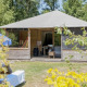 Træhytte med overdækket terrasse og hængekøje på græsplæne, Camphome lodge, omgivet af træer.