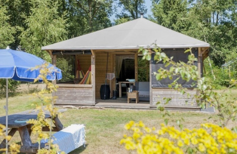 Houten lodge genaamd Camphome met overdekte veranda en hangmat, op gras en omringd door bomen.