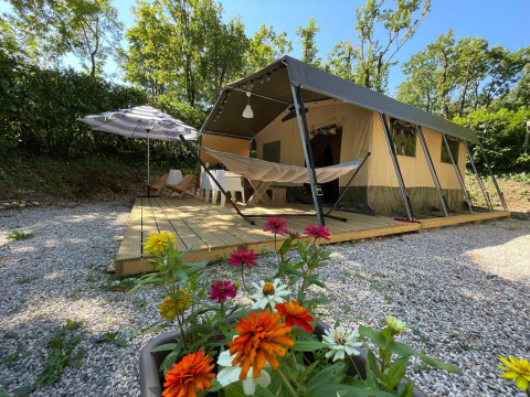 Safari tent Base Lodge met hangmat, bloemen en houten terras, omgeven door groene bomen.