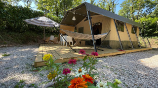 Tienda safari Base Lodge con hamaca, maceta de flores y terraza de madera rodeada de árboles verdes.