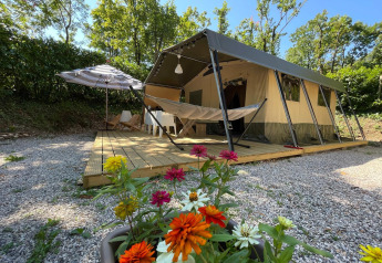 Tienda safari Base Lodge con hamaca, maceta de flores y terraza de madera rodeada de árboles verdes.