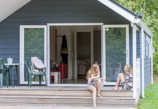 Deux filles discutent devant un chalet avec véranda au parc de vacances Witterzomer aux Pays-Bas.