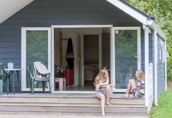 To piger sidder og taler foran en chalet med veranda i Holiday park Witterzomer, Holland.
