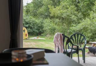 Vista desde un chalet con veranda hacia el jardín, sillas de plástico y parque infantil en Witterzomer.