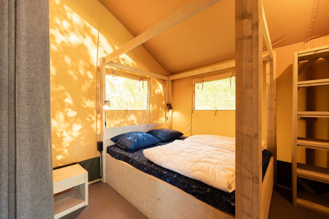 Vista interior de una tienda safari con cama doble y estructura de madera en Villatent Nomad, Vakantiepark de Twee Bruggen.