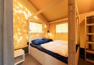 Vista interior de una tienda safari con cama doble y estructura de madera en Villatent Nomad, Vakantiepark de Twee Bruggen.