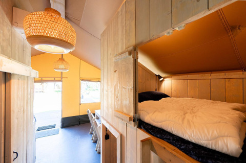 Interior de la tienda safari Villatent Nomad con cama elevada y comedor en Vakantiepark de Twee Bruggen.