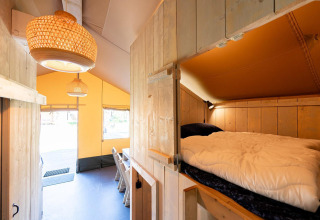 Interior de la tienda safari Villatent Nomad con cama elevada y comedor en Vakantiepark de Twee Bruggen.