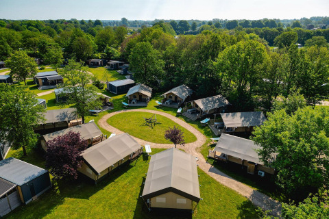 Vista aérea de tiendas safari en Villatent Nomad en Vakantiepark de Twee Bruggen, Países Bajos, rodeadas de árboles.