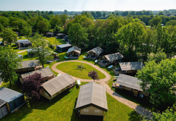 Vista aérea de tiendas safari en Villatent Nomad en Vakantiepark de Twee Bruggen, Países Bajos, rodeadas de árboles.