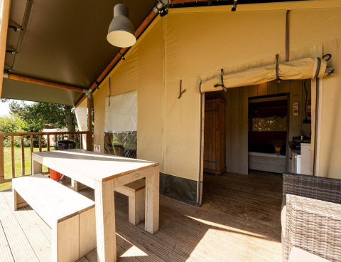 Safari-Zelt Villatent Wood mit Holztisch, Bänken, Terrasse und Blick ins offene Zeltinnere.