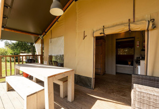 Safari-Zelt Villatent Wood mit Holztisch, Bänken, Terrasse und Blick ins offene Zeltinnere.