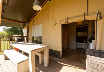 Tente safari Villatent Wood avec table extérieure, entrée ouverte et terrasse en bois ensoleillée.