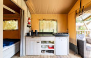 Area cucina di una tenda safari con fornello, mini-frigo, armadi e vista sul terrazzo a Villatent Wood.
