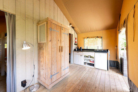 Binnenzicht van Villatent Wood safaritent met houten meubels, compacte keuken en lamp.