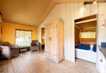 Innenraum des Safari-Zeltes Villatent Wood mit Holzmöbeln, Korbstühlen und Schlafbereich.
