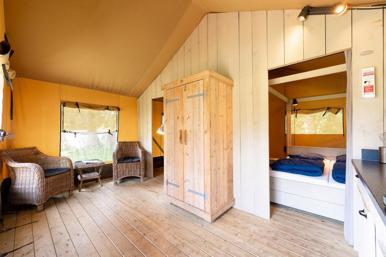 Interior of Villatent Wood safari tent, featuring wooden furniture, wicker chairs, and sleeping area.
