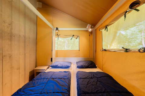 Intérieur d'une tente safari Villatent Wood avec deux lits simples, draps bleus et murs jaunes en toile.