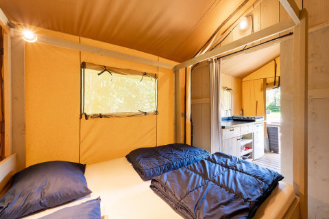 Vista interior de una tienda safari Villatent Wood con cama doble, cocina pequeña y luz acogedora.