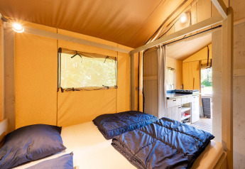 Vista interna di una tenda safari Villatent Wood con letto matrimoniale, angolo cottura e illuminazione calda.