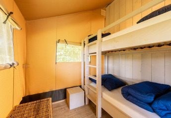 Interno di una tenda safari chiamata Villatent Wood con letto a castello, pavimento in legno e pareti gialle.