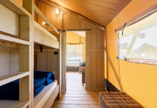 Interieur van een Villatent Wood safaritent met stapelbedden, houten vloer en grote ramen.