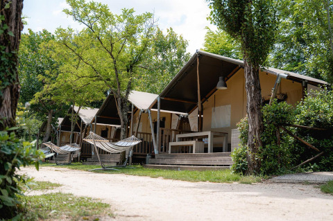 Tienda safari Villatent Wood en Camping Il Poggetto, Italia, con hamacas y árboles frente a las tiendas.