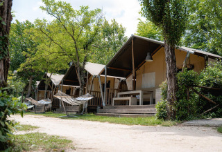 Tienda safari Villatent Wood en Camping Il Poggetto, Italia, con hamacas y árboles frente a las tiendas.