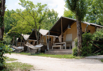 Safari-Zelte Villatent Wood auf Camping Il Poggetto in Italien mit Hängematten und Bäumen davor.