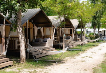 Safari-Zelte mit Veranden und Hängematten bei Camping Il Poggetto in Italien, umgeben von Bäumen.