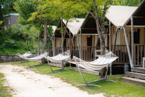Tiendas safari en Camping Il Poggetto, Italia, con hamacas bajo árboles en un entorno soleado y tranquilo.