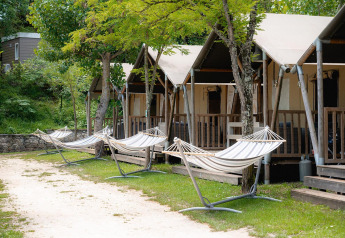 Safari-Zelte im Camping Il Poggetto, Italien, mit Hängematten unter Bäumen in entspannter Atmosphäre.