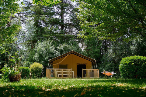 Tienda safari Villatent Wood en Camping Lestaubière, Francia, rodeada de árboles y césped verde.