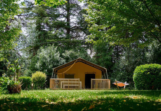 Tienda safari Villatent Wood en Camping Lestaubière, Francia, rodeada de árboles y césped verde.