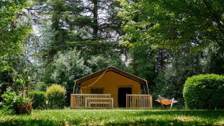 Tienda safari Villatent Wood en Camping Lestaubière, Francia, rodeada de árboles y césped verde.