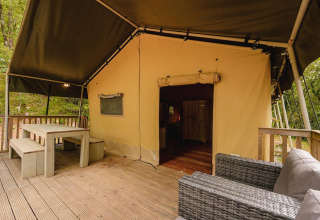 Tenda safari Villatent Wood al Camping Lestaubière in Francia con veranda in legno, divano e tavolo.