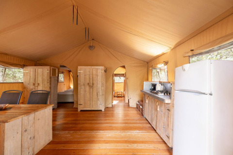 Vista interior de una tienda safari Villatent Wood en Camping Lestaubière en Francia con cocina y mobiliario.