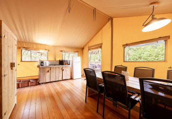 Interno di una tenda safari Villatent Wood al Camping Lestaubière in Francia, con zona pranzo e angolo cottura.