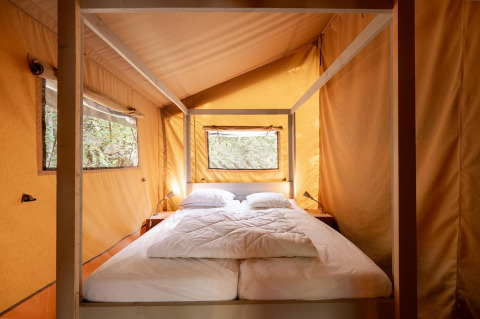 Vista interior de una tienda safari Villatent Wood con cama doble en Camping Lestaubière, Francia.