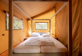 Interieur van een Villatent Wood safaritent met tweepersoonsbed op Camping Lestaubière in Frankrijk.