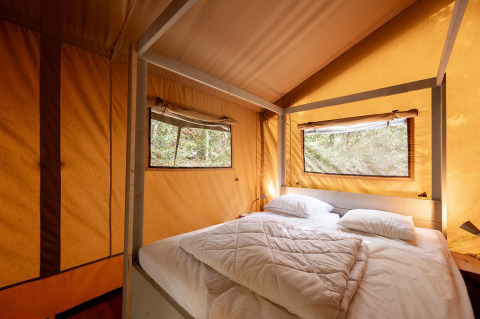 Vista interior de una tienda safari Villatent Wood con cama doble, dos ventanas y luz natural.