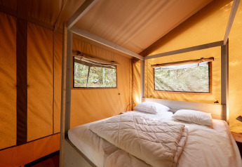 Interno di una tenda safari Villatent Wood con letto matrimoniale, due finestre e luce naturale.