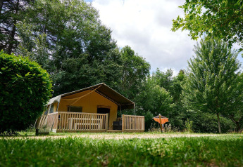 Tienda safari Villatent Wood con terraza de madera en Camping Lestaubière, Francia, entre árboles y césped verde.