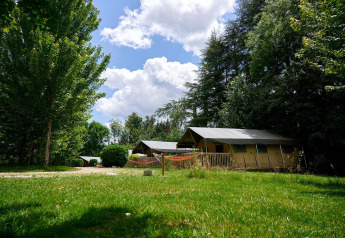 Safari tent Villatent Wood at Camping Lestaubière in France, surrounded by lush greenery and trees on a sunny day.
