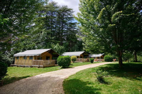 Tiendas safari en Villatent Wood en Camping Lestaubière, Francia, rodeadas de árboles y vegetación.