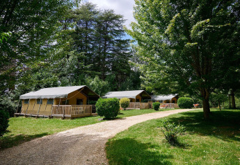 Safari tents at Villatent Wood, Camping Lestaubière, France, surrounded by greenery and tall trees.