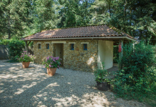 Stone building with a tiled roof at Camping Lestaubière in France, surrounded by trees and potted flowers.